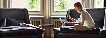 Gastherme mit Warmwasserspeicher: Frau sitzt vor einem Fenster im Wohnzimmer auf einer Couch und studiert Unterlagen.